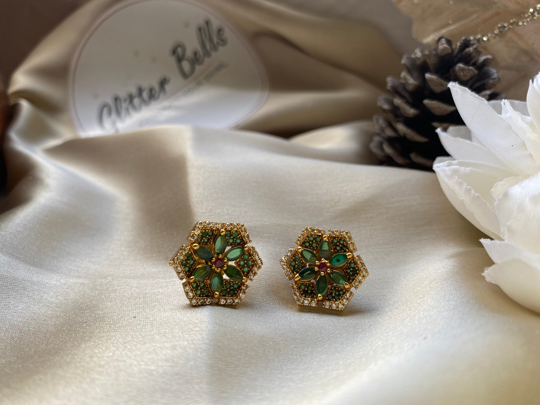 Hexagonal earrings with green gemstones on a white fabric background