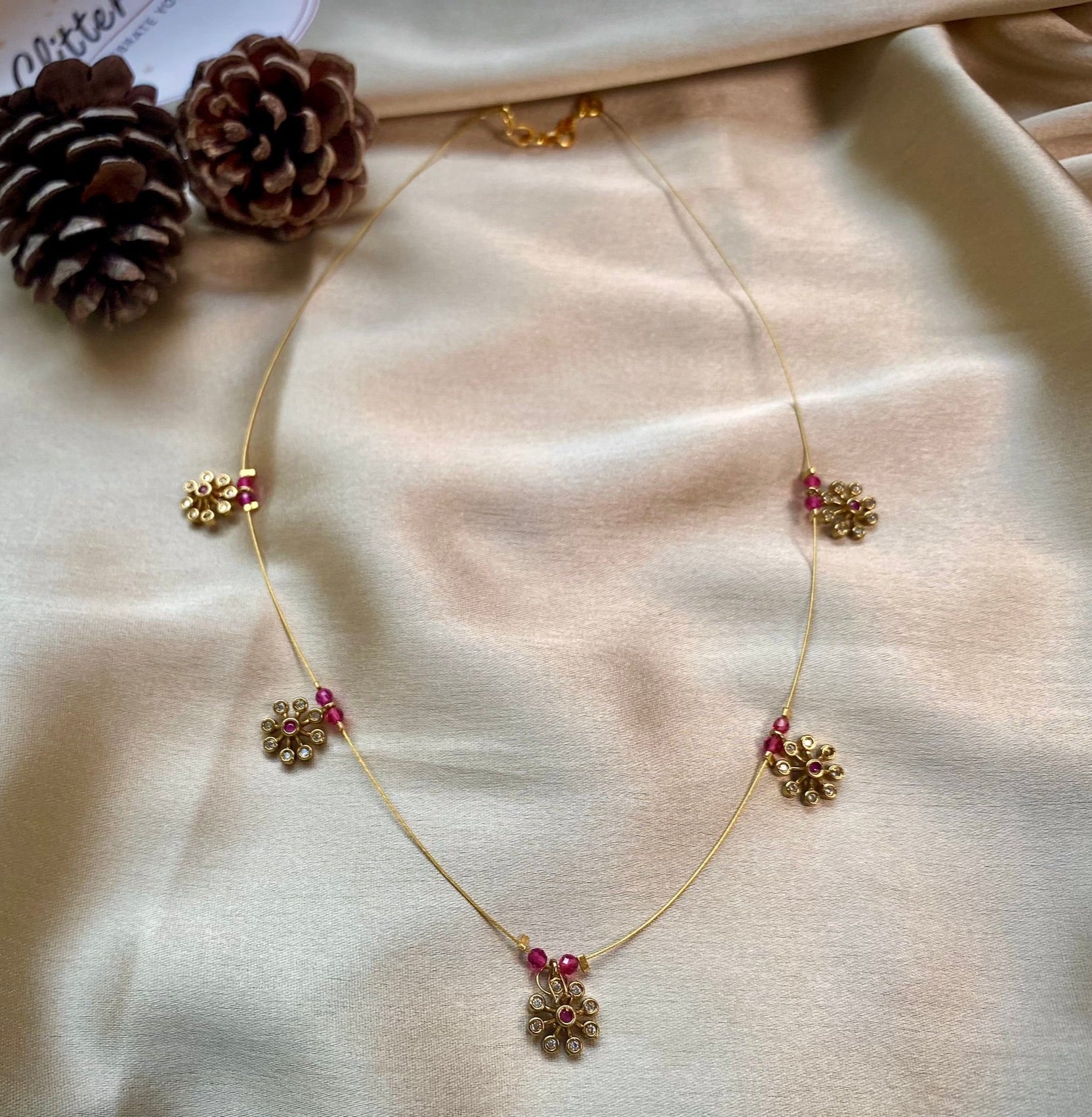Delicate gold-plated chain with floral motifs. Accented with ruby-pink beads for a pop of color. 